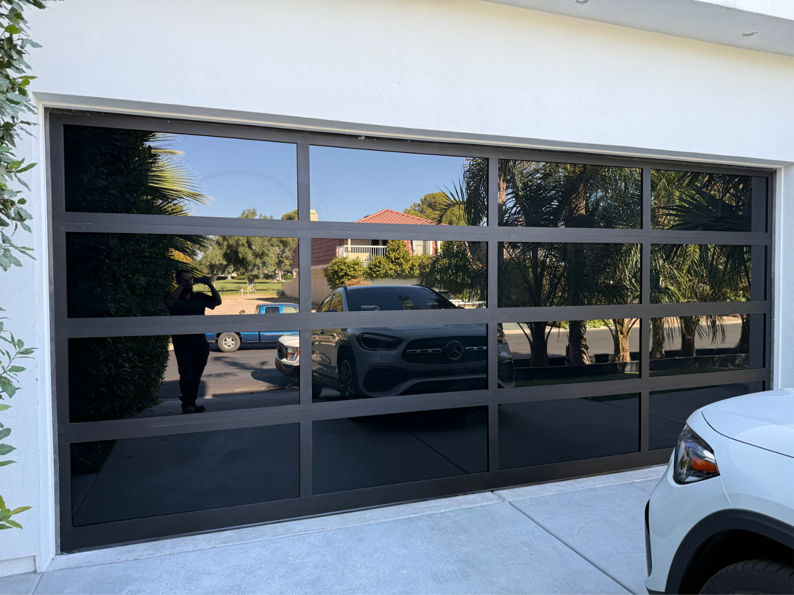 Installed dark tinted full-view glass garage door reflecting a car and street